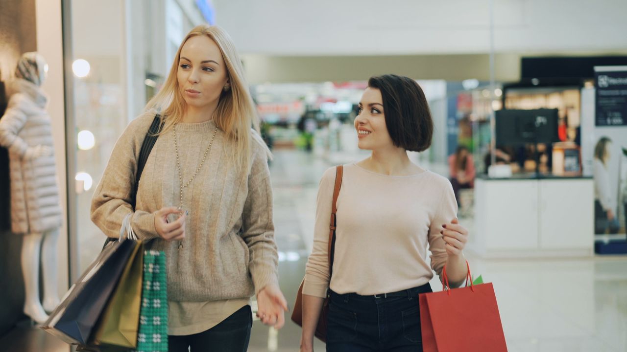 Two women shopping in a mall, carrying bags and enjoying leisure time.