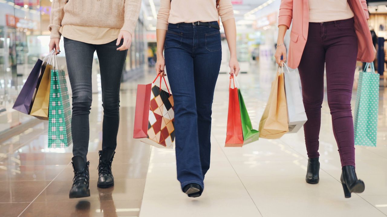Three women walking in a mall, holding colorful shopping bags.